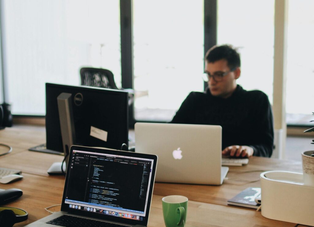 A web developer working on code in a modern office setting with multiple devices.